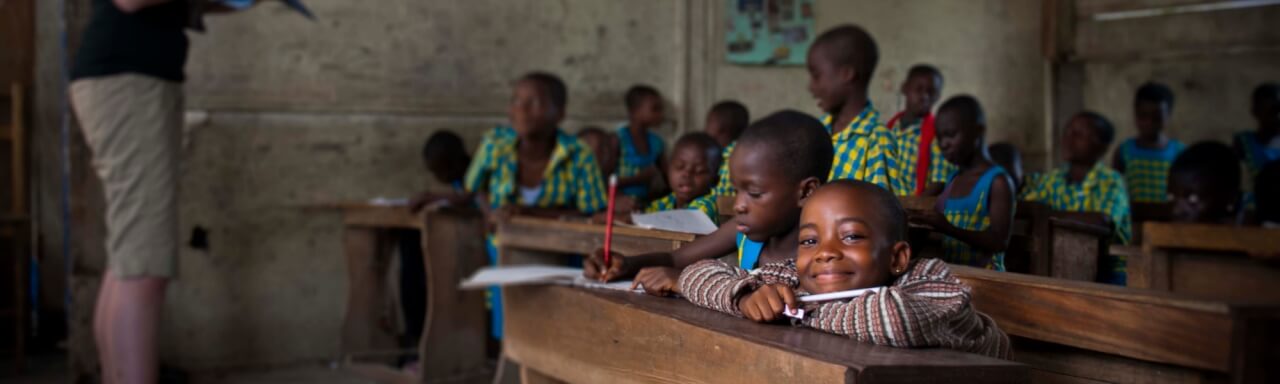 Children in dirt-floor school room listening to teacher